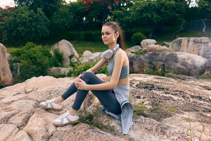 Young woman in activewear sitting on rocky terrain, expressing determination and focus in a vibrant outdoor setting, conveying a healthy lifestyle and fitness mindset
