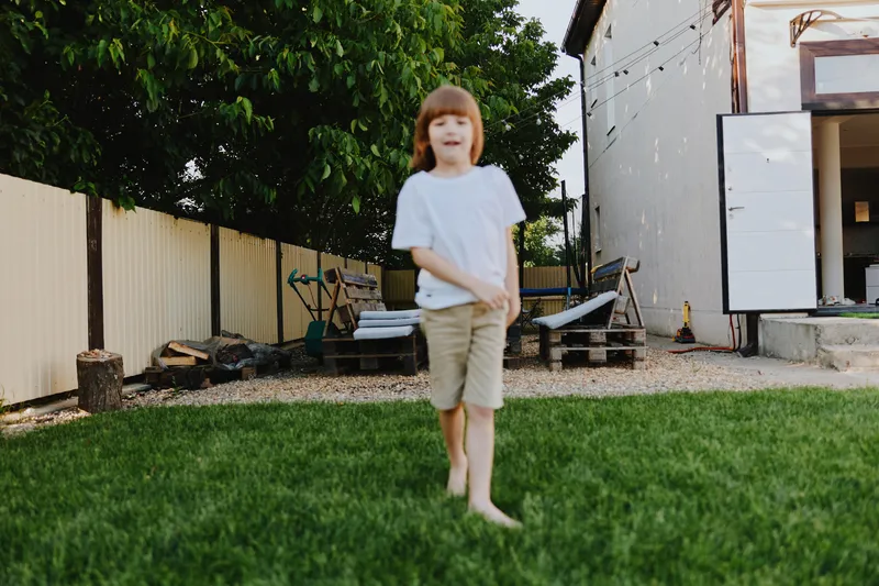 Happy boy playing outdoors in a sunny garden, enjoying freedom and nature. The green grass and quiet ambiance create a perfect playground for children. ###