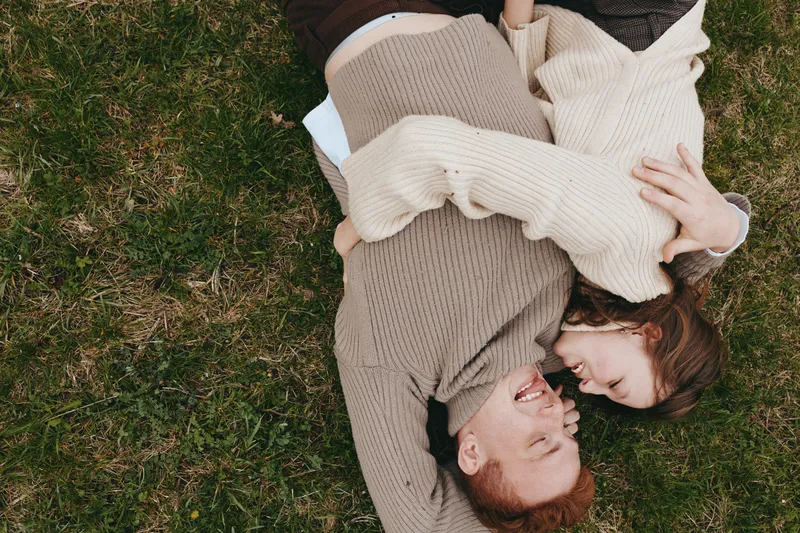 Couple embrace cuddle sweaters grass outdoor love smile warmth candid moment as they lie together in cozy clothes enjoying outdoor lifestyle in warm afternoon light with relaxed faces and gentle