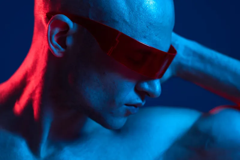 A captivating image of a man with a bald head wearing futuristic red sunglasses, showcasing a striking blue background and dramatic lighting that enhances the mood.