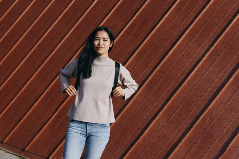 Woman, backpack, casual, street, outdoor, fashion, standing against a diagonal wooden wall, this urban style shot captures a confident, relaxed pose and everyday clothing suitable for travel, campus,
