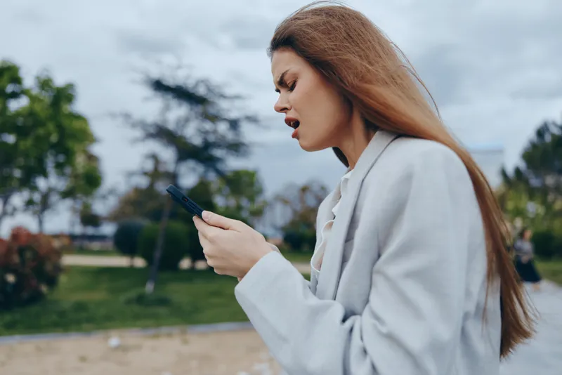 frustrated woman with smartphone outdoors experiencing financial crisis and stock market loss in casual coat with long hair