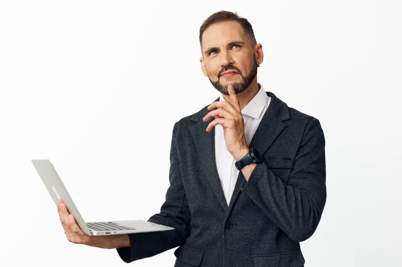 A professional businessman stands with a laptop, displaying a thoughtful expression, set against an isolated colored background to clearly convey focus, confidence, and advanced expertise.