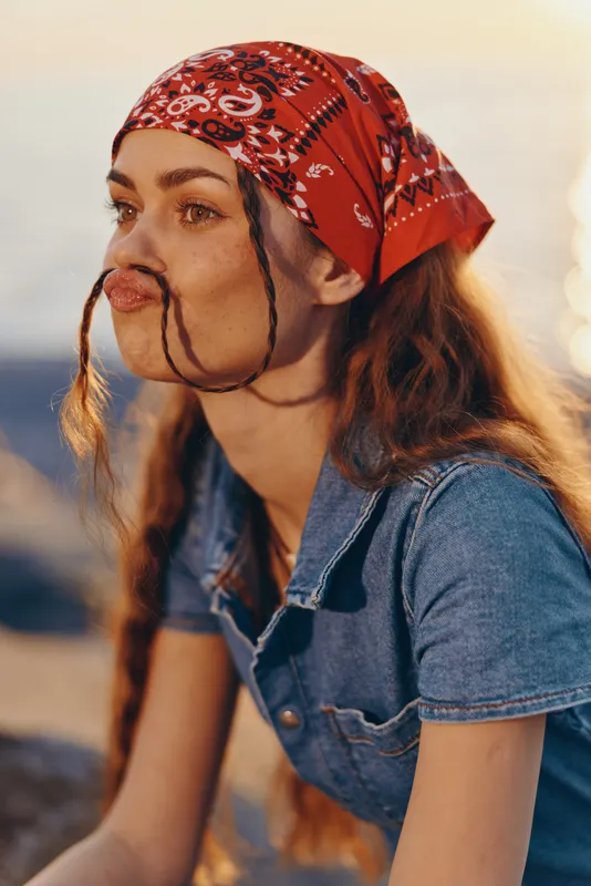 lifestyle woman in modern boho-western denim street style wearing a red bandana with natural light and film color tones, expressive and relaxed mood outdoors