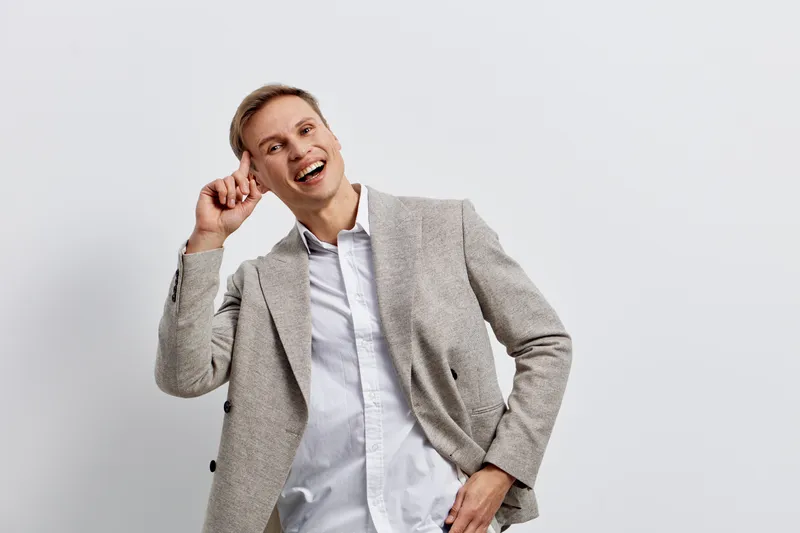Jovial smiling man with light brown hair wearing casual gray blazer and white shirt, posing against plain white background, cheerful expression, candid shot, lifestyle concept, close-up portrait.