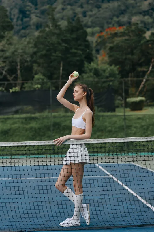 Young athletic woman in sportswear preparing to serve a tennis ball on a court, showcasing determination and focus in a vibrant outdoor setting