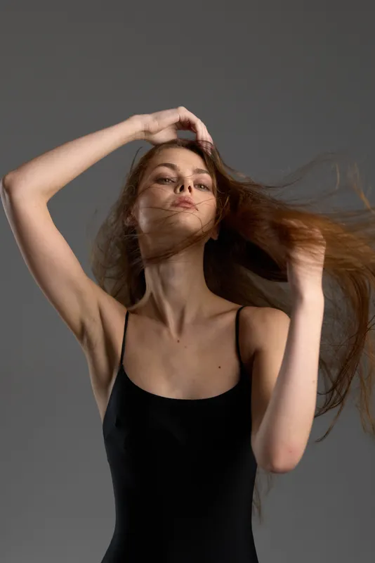 Elegant woman with flowing hair posing in black dress with confident expression in neutral studio lighting.