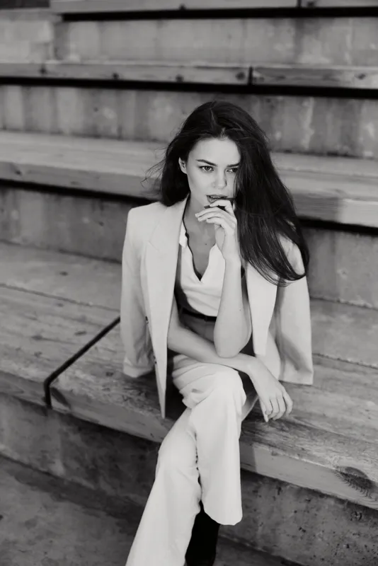 Confident woman in a tailored business outfit seated on steps, showcasing modern style and professionalism, exuding elegance and poise in monochrome colors.
