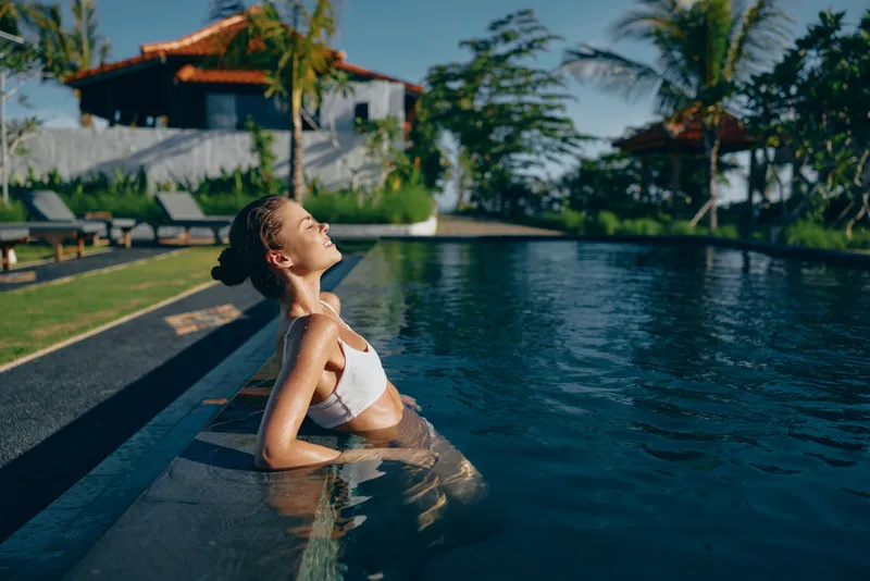 A woman in a white bikini lounges in a sunny pool, shoulders relaxed, enjoying warm weather. A tranquil lifestyle moment that conveys relaxation, vacation vibes, and resort comfort for a lifestyle