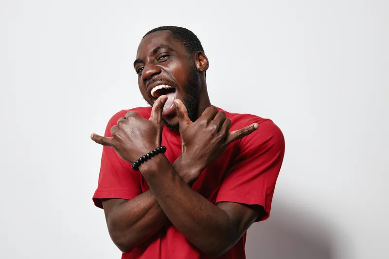 African American man with dark skin wearing red t shirt posing with expressive hands and joyful face on white background. Casual style and confident mood in studio portrait.