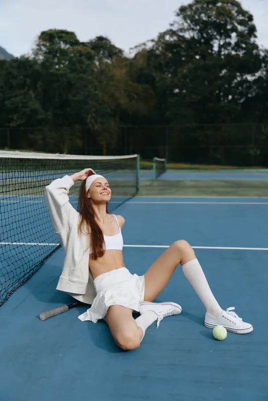 Young female athlete enjoying a break on the tennis court, wearing sporty attire and a joyful expression, showcasing vibrant colors and a dynamic outdoor setting