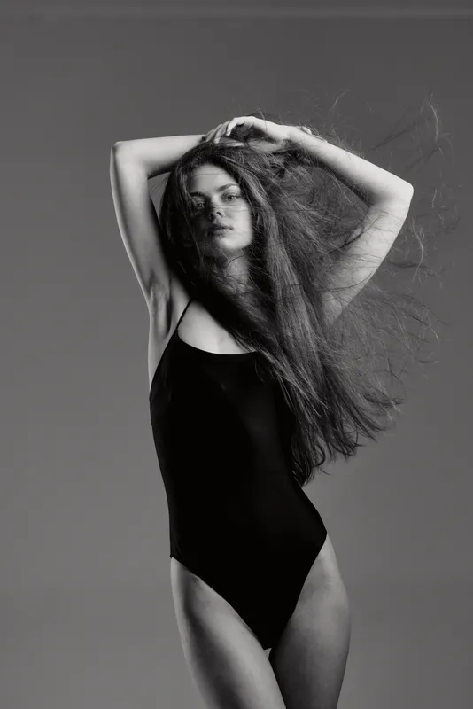 Black and white portrait of a young woman with flowing hair in a black swimsuit expressing elegance and movement.