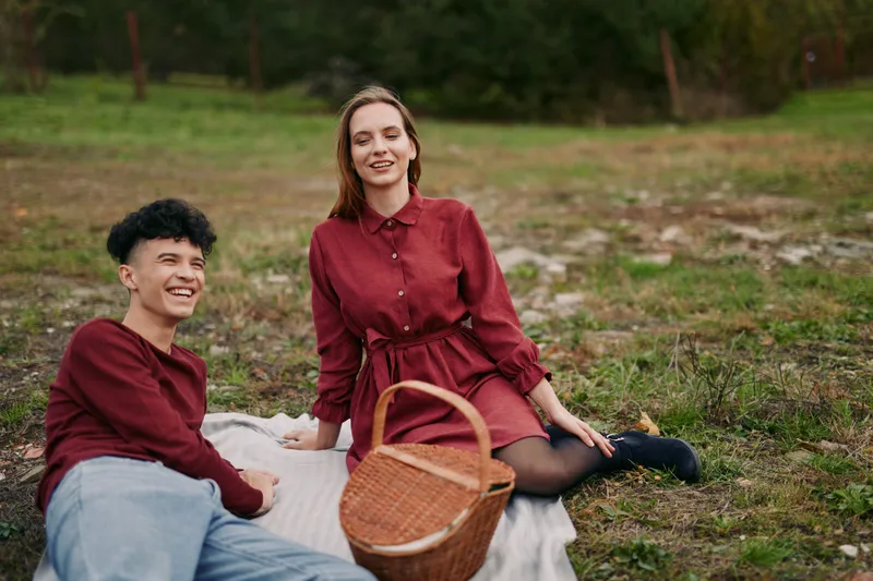 A young couple enjoying a relaxed picnic on a blanket in a meadow, sharing authentic, genuine moments of laughter and close connection captured in a candid, realistic storytelling style.