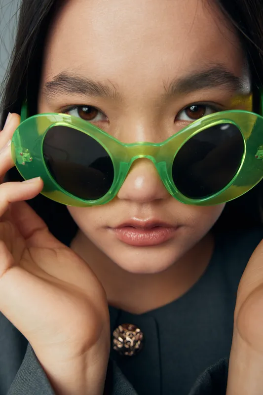Woman with green sunglasses and serious expression closeup face portrait fashion style, black outfit and natural makeup with intense eyes looking at camera for beauty concept.