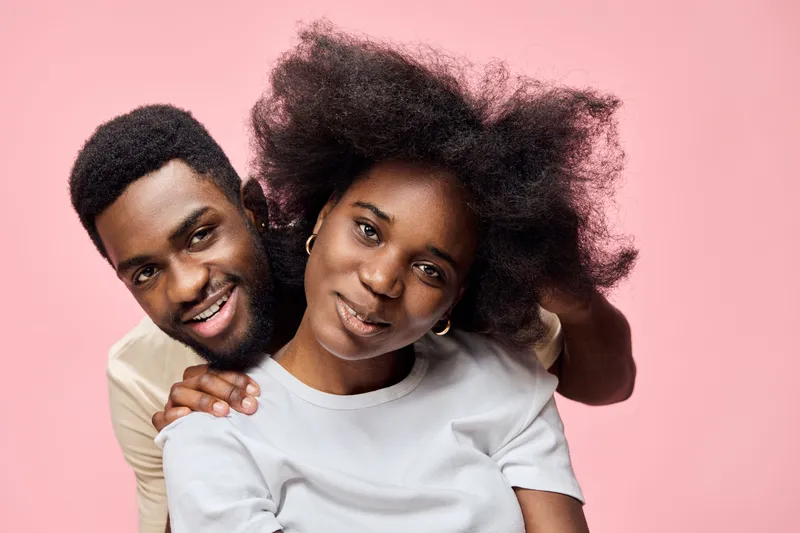 Joyful couple portrait with natural hairstyles against a pink background, showcasing love and connection, perfect for lifestyle and relationship themes