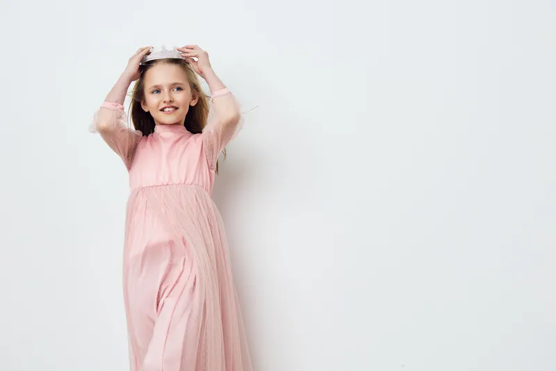 Happy girl in a pink dress with a crown, celebrating joy and innocence against a light background, ideal for children s fashion and birthday themes