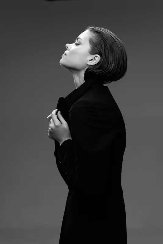 Black and white profile of a thoughtful woman wearing a dark coat with a serene expression and short hair.