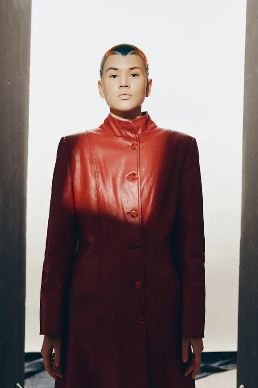 woman in red leather coat with colorful short hair standing strong, minimalist background, modern fashion, serious expression, sharp lighting