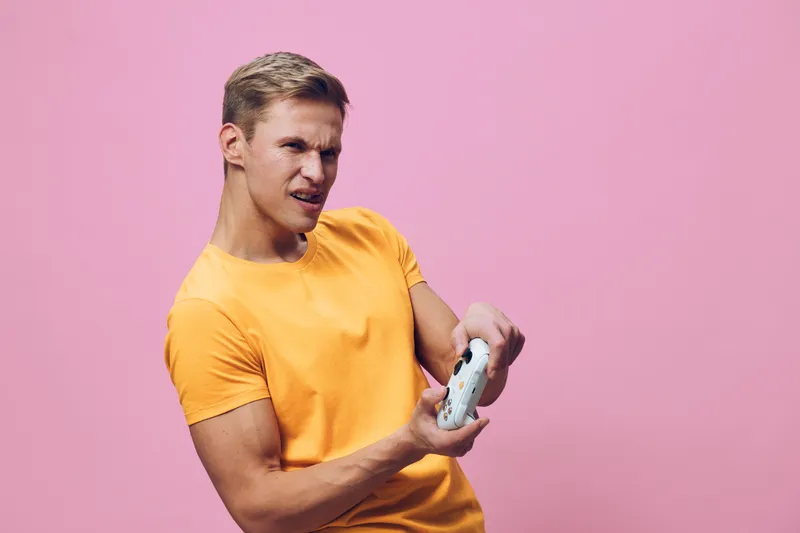 focused young caucasian man wear orange tshirt play video game hold controller isolated pink background digital entertainment concept