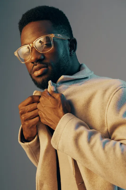 Stylish man in glasses adjusting his coat with a confident expression, showcasing contemporary fashion trends and vibrant colors
