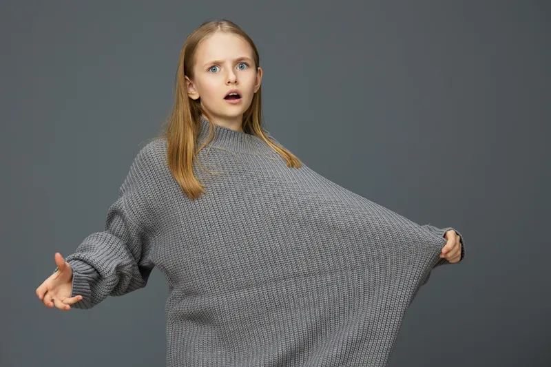 Surprised young girl in oversized gray sweater expressing shock against a neutral background Emotion, style, and winter fashion highlight youth and comfort