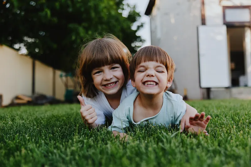 Happy children playing on green grass, showcasing joyful expressions and a playful atmosphere in a sunny garden setting.