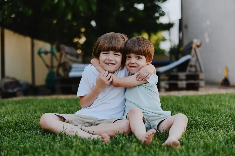 Two smiling boys enjoying a sunny day outside, showcasing friendship and joy in a green yard with playful happiness and carefree spirit.
