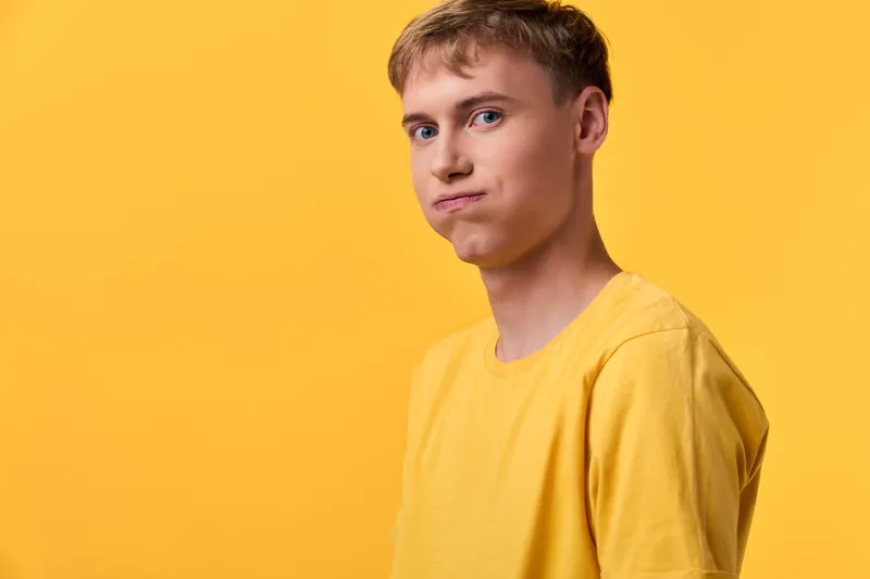 Confused male in a yellow shirt stands against a yellow backdrop, conveying uncertainty and casual style for fashion, emotion and advertising campaigns in a studio setting