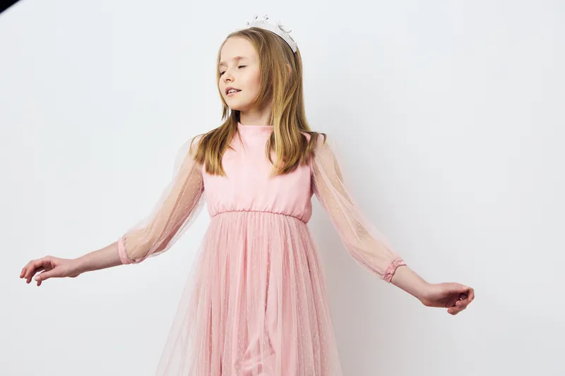 A joyful girl in a pink tulle dress with a crown, celebrating in a dreamy setting, embodying happiness and innocence with soft pastel colors