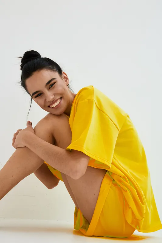 smiling woman in yellow casual clothing sitting with knees hugged, relaxed and happy, bright color, minimalistic background, natural light portrait