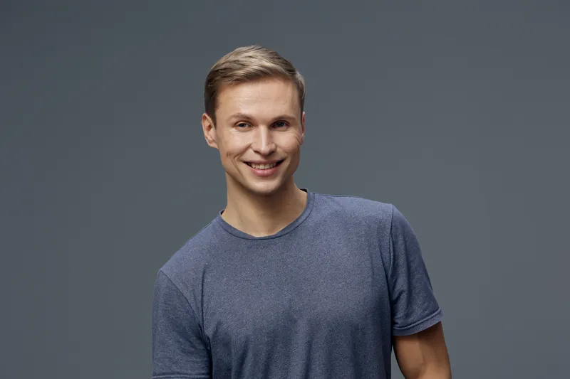 Smiling young man with short blond hair wearing casual blue t-shirt looking at camera with cheerful expression isolated on plain gray background studio portrait. People lifestyle concept