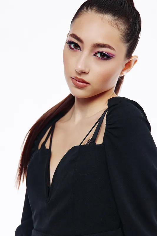 Young woman with creative vibrant makeup and pink eyeliner wearing a black fashion top poses in studio light. Beauty concept exploring fashion and artistic expression close-up portrait.