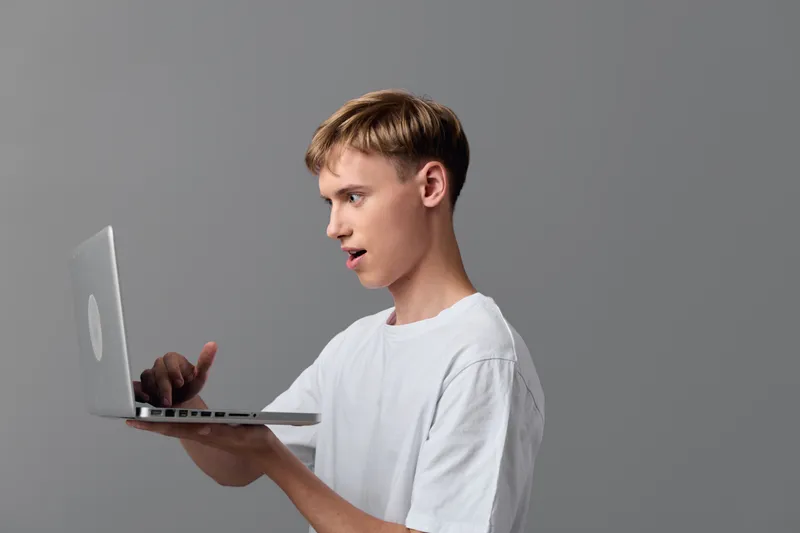 Man typing on a laptop computer in a minimalist studio, focused on the screen, illustrating online work, learning, and modern technology with casual attire.