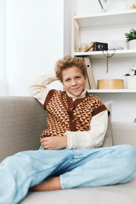 Authentic scene of a playful student at home, a young boy relaxing on a sofa in a cozy school inspired outfit, embodying natural lifestyle and childhood charm.