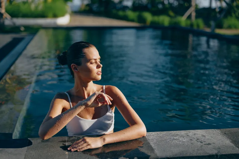 Young woman relaxing in outdoor pool during sunny day, enjoying lifestyle moment with closed eyes and calm expression. Concept of wellness, leisure, and summer relaxation.