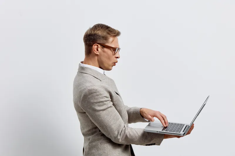 surprised man holding laptop wear glasses gray blazer white background digital nomad technology concept