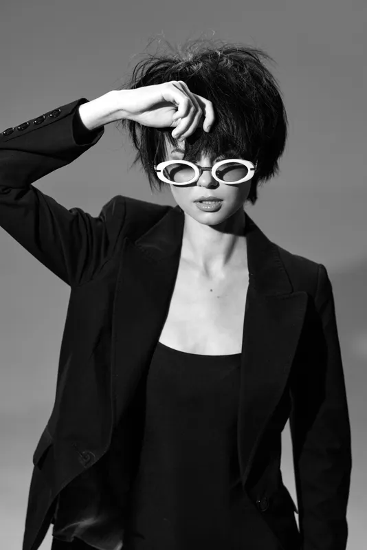 Black and white portrait of stylish woman with sunglasses in black blazer showing confident pose.