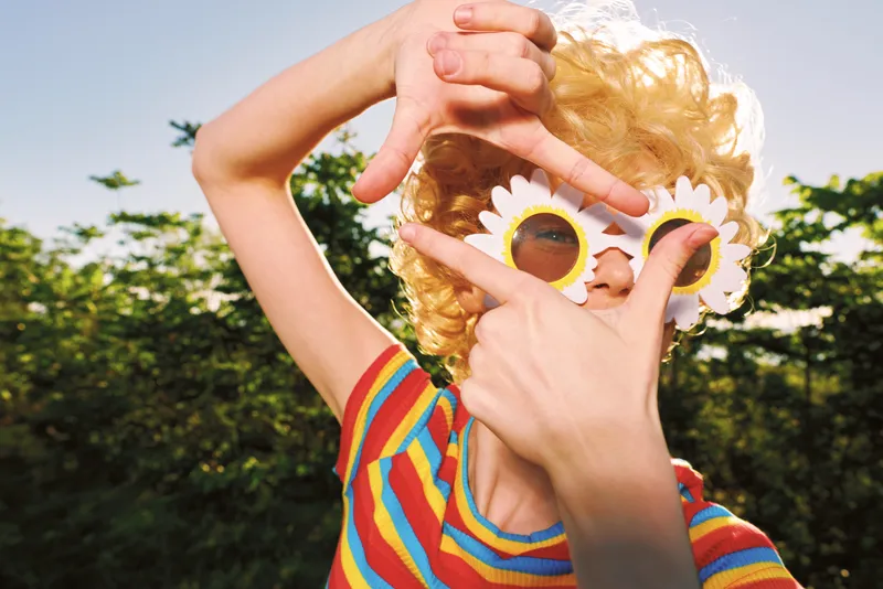 Child wearing floral sunglasses outdoors on a sunny day, captured in retro film tones, conveying playful imagination and carefree mood, bright colors and warm light enhance summer fun.