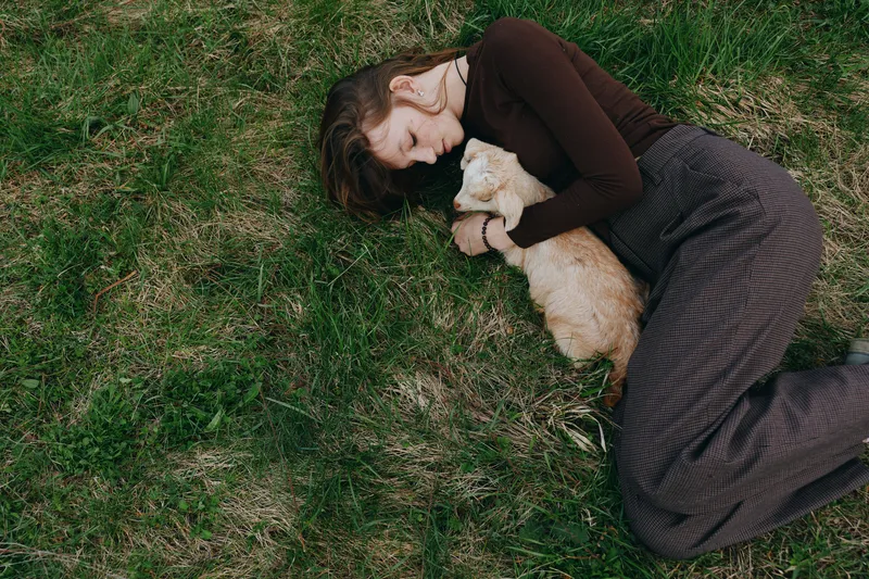 A relaxation moment as a compassionate human rests beside a small animal on green grass, enjoying a calm outdoors moment. A lifestyle scene highlighting companionship, care, and healing through touch.