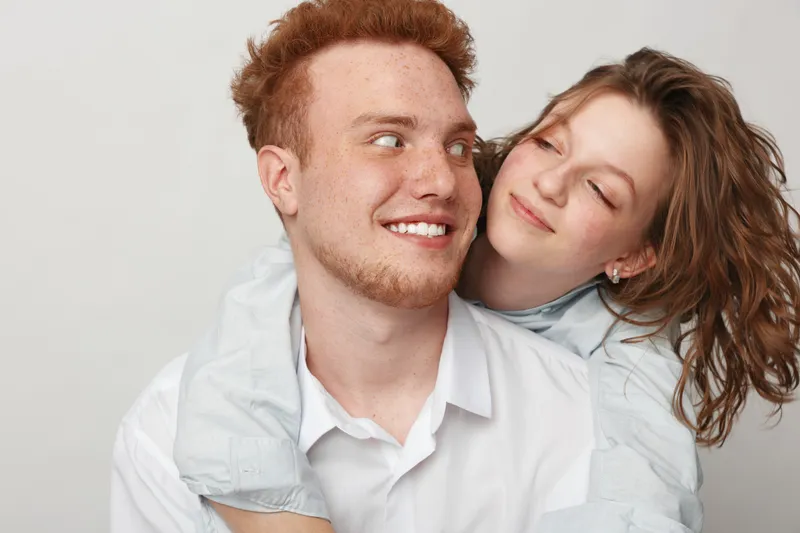 Happy young couple with red hair and curly hair smiling and embracing each other on white background. Concept of love, relationship, friendship, and positive emotions.