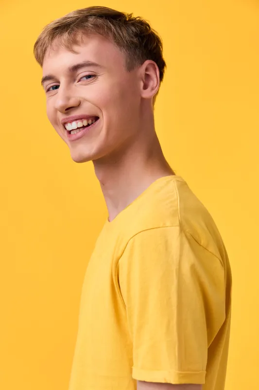 Smiling man in a yellow t shirt against a vibrant yellow studio background, showcasing casual style, positive expression, relaxed pose, bright tone and approachable mood for lifestyle or fashion stock