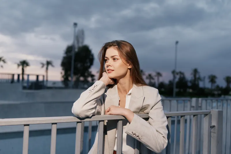 Young woman in light beige suit thoughtfully looking away outdoors at sunset, casual fashion style, autumn urban background, confident woman portrait