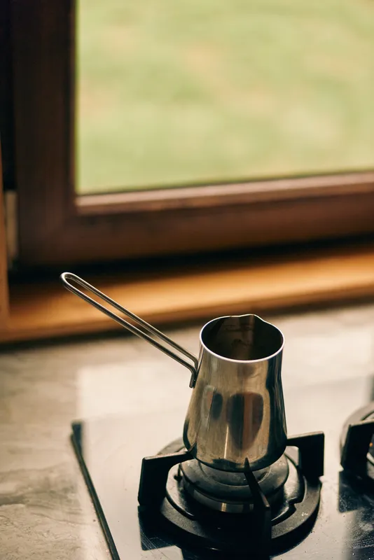 Stove burner closeup with a metal kettle on a gas hob, silver steel surface reflecting light, capturing domestic cooking and kitchen use, showcasing daily use.