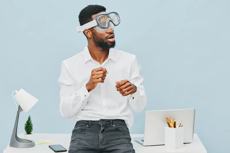 Professional black man in white shirt wearing safety goggles, demonstrating scientific experiment or concept with focused expression, modern office background, flat lay setup, educational and innovati