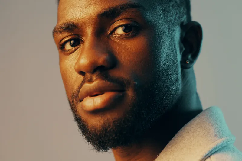 Portrait of a confident Black male model with a stylish haircut, showcasing warm skin tones and thoughtful expression, against a soft gradient backdrop
