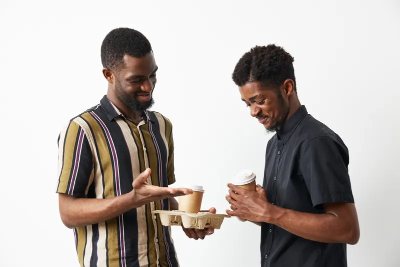 Two African American men enjoying coffee together, sharing laughter and conversation, dressed casually in stylish shirts, highlighting friendship and joy.