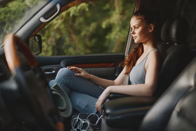 Young woman in casual outfit reflecting on life while sitting in a parked car surrounded by nature Relaxed mood and natural light enhance the scene
