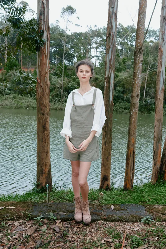 Young woman in a stylish casual outfit standing by a serene lake surrounded by trees, evoking a peaceful and nature inspired vibe