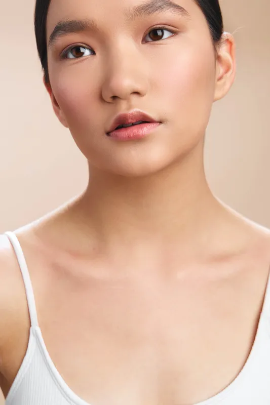 Asian woman gazes softly into the camera, presenting a calm and confident presence in a clean studio portrait that emphasizes natural beauty and poised expression.
