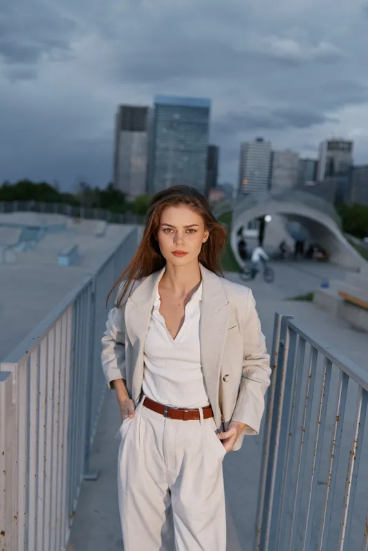 Confident woman in beige business suit standing outdoors with urban skyline background, showcasing professional style and determination